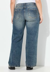 Vaqueros de mezclilla azul claro con piernas anchas, que cuentan con patrones decorativos de estrellas en los bolsillos traseros y un diseño clásico de cinco bolsillos.