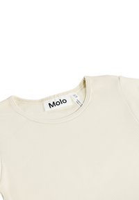 Kremno obarvan žametast top z okroglo izrezom in kratkimi rokavi. Na vratu je vidna oznaka z logotipom, priložena pa je tudi oznaka velikosti.