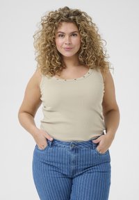 Beige ribbattu tank top, jossa on koristeelliset metallikoristeet kaula-aukossa, yhdistettynä sinisiin pystysuoriin korkeavyötäröisiin farkkuihin.