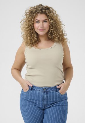 Beige gerippter Tanktop mit dekorativen Metallakzenten am Ausschnitt, kombiniert mit blauen hochtaillierten Jeans mit vertikalen Streifen.