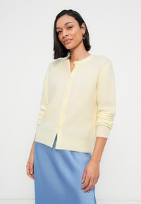 Ανοιχτό κίτρινο ζακέτα από απαλό ύφασμα, με μακριά μανίκια, στρογγυλή λαιμόκοψη και κουμπιά στο μπροστινό μέρος. Λείο ύφασμα.