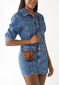 Ensemble en jean bleu composé d'une chemise et d'une jupe avec un ourlet effiloché. Petit sac en cuir marron à bandoulière avec un rabat et des détails de couture.