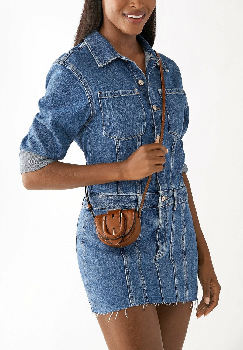 Ensemble en jean bleu composé d'une chemise et d'une jupe avec un ourlet effiloché. Petit sac en cuir marron à bandoulière avec un rabat et des détails de couture.