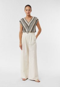 Zwart-wit zigzagpatroon top met een V-hals, gecombineerd met crème wijdvallende broeken en tan gekruiste sandalen. Eenvoudig riemdetail inbegrepen.