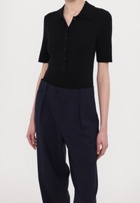 Czarny prążkowany polo z krótkim rękawem i plisą na guziki, zestawiony z spodniami w kolorze granatowym o wysokim stanie z detalem w postaci guzika z boku.