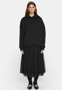 Czarna, oversize bluza z miękkiej tekstury, połączona z czarną, warstwową spódnicą z tiulu. Zawiera ściągacze na mankietach oraz drapowany dekolt.