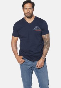 Navy V-neck t-shirt made of cotton with short sleeves, featuring a mountain graphic in blue and orange on the chest and tattooed arms.
