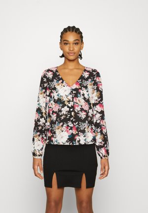 Blusa preta floral com mangas longas, apresentando flores multicoloridas e detalhe de botões, combinada com uma saia preta com fendas laterais.