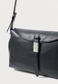 Schwarze Leder Schultertasche mit Klappverschluss, ausgestattet mit einem silbernen Akzent mit dem Wort "PINKO" und einem verstellbaren Tragegurt. Glatte Textur.