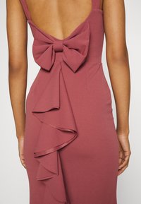 Himbeer-pinkes, figurbetontes Kleid mit tiefem Rückenausschnitt, das eine große Schleife und eine seitliche, kaskadierende Rüsche aufweist, gefertigt aus einem glatten Stoff.