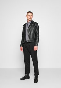 Giacca da biker in pelle nera, camicia grigia con bottoni, pantaloni neri, stivali neri alla caviglia. Design minimalista, texture liscia, vestibilità su misura.
