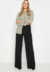 Pantalones de pierna ancha negros combinados con una camisa de botones a rayas beige de manga larga y cuello clásico.