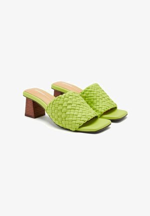 Sandalias deslizantes verdes tejidas con punta cuadrada y un bajo tacón de bloque de madera. La parte superior presenta un diseño de trenzado texturizado.