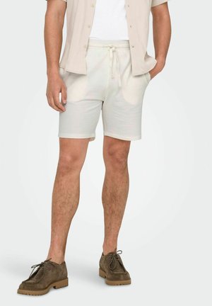 Beige, gestructureerde shorts met een elastische tailleband en een trekkoord. Gecombineerd met een beige shirt met korte mouwen en bruine suède schoenen.