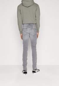 Jeans de mezclilla grises con detalles de costura en los bolsillos traseros, combinados con un sudadera verde y zapatillas negras, vistos desde atrás.