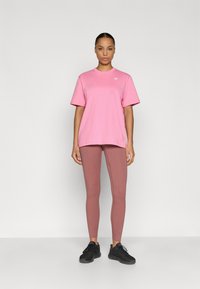 Ružové oversized tričko s krátkymi rukávmi, doplnené priliehavými legínami v ružovej farbe a čiernou športovou obuvou. Minimalistický dizajn a hladká textúra.