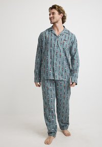 Men's cotton pajama set in teal, featuring a nutcracker pattern. Includes a button-up top and matching pants with an elastic waistband.