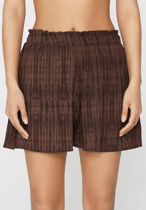 Femme portant un short plissé taille haute de couleur marron foncé avec une ceinture élastique et une texture verticale subtile.