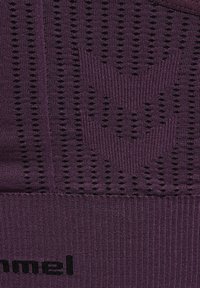 Lilla strikket stof med sorte ventilationshuller, der danner Hummel-logoet og brandnavnet "hummel" nederst.