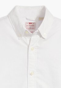 Bílá košile Levi's s knoflíkovým límcem a viditelnou etiketou uvnitř límce.