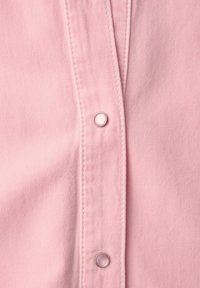 Gros plan sur un tissu rose avec deux boutons-pression argentés alignés verticalement sur une couture pliée.