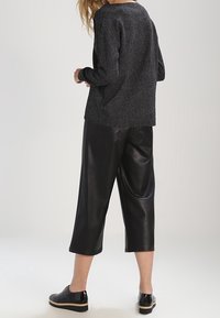 Schwarzer Wollpullover und schwarze, cropped Lederhosen, beide mit lockerer Passform. Schwarze Schuhe mit beiger Sohle runden das Outfit ab.