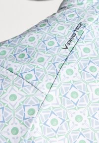 Detail bílé látky s geometrickým vzorem golfového tématu v zelené a modré barvě a černým logem "SWING TECH".