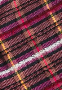 Det vävda tyget har ett rutig mönster med rosa, svart, gult och röda linjer. Texturen ser något lurvig ut, med trasiga kanter.