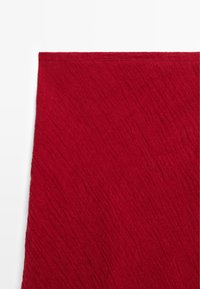 Czerwona tkanina o fakturze zgniecionej, pomarszczonej oraz z prostym przeszyciem wzdłuż górnej krawędzi.