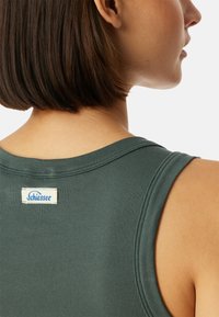 Mörkgrön ribbad tanktop med rundad halsringning och vida ärmhål. Har en vit etikett med blå text på baksidan.