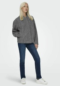 Grå ullblandad jacka med hög krage och avslappnad passform, kombinerad med mörkblå jeans och vita sneakers.
