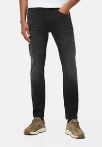Schwarze Denim-Jeans mit einem schmalen Schnitt, im Fünf-Taschen-Stil und subtiler verblasster Textur, kombiniert mit braunen Sneakern.