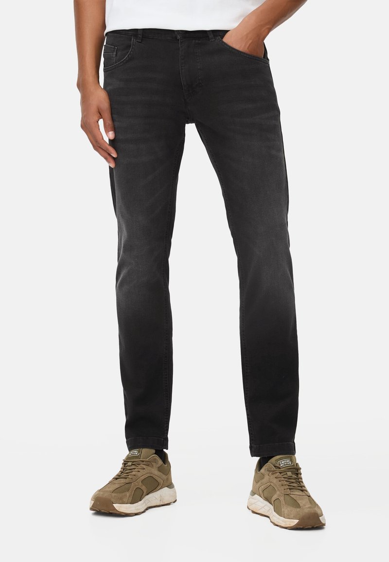 Schwarze Denim-Jeans mit einem schmalen Schnitt, im Fünf-Taschen-Stil und subtiler verblasster Textur, kombiniert mit braunen Sneakern.