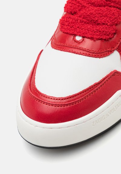 Red leather sneaker with white accents, textured red laces, and a smooth toe cap. Features subtle branding on the side and a durable sole.