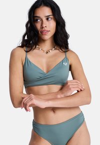 Ensemble bikini vert comprenant un haut style cache-cœur avec des bretelles fines et un bas assorti taille basse. Le tissu semble lisse avec peu d'accents.