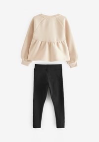 Felpa rosa chiaro con base a peplo e maniche lunghe, abbinata a leggings neri realizzati in un materiale liscio ed elasticizzato.