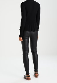 Svart ribbad långärmad topp med peplumkjol, matchad med figurnära svarta läderbyxor och bruna sandaler med remdesign.