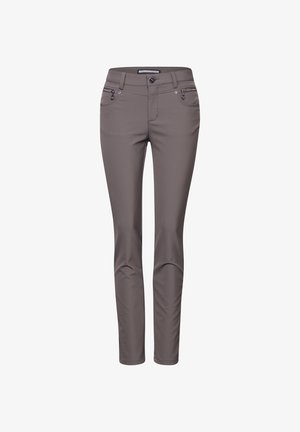 Un pull en laine beige et duveteux superposé sur une chemise blanche, associé à un pantalon gris ajusté et des bottines noires. Design concis aux lignes simples.
