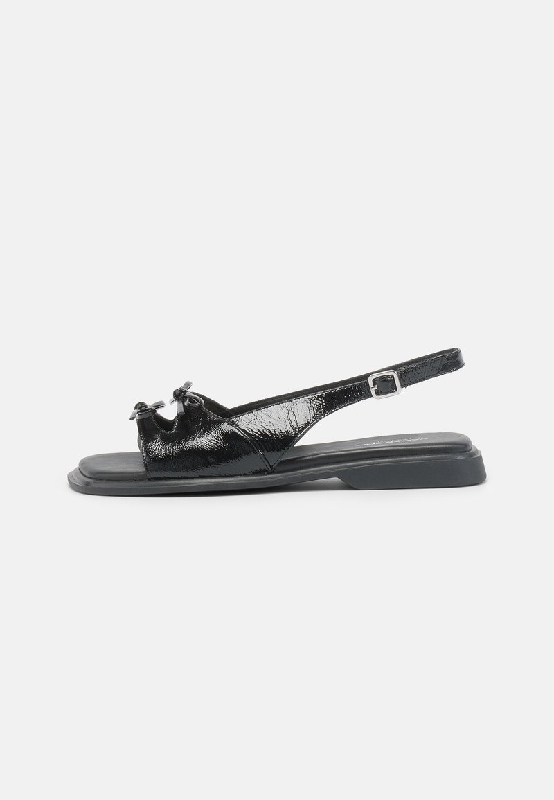 Sandale plate en cuir verni noir avec bout ouvert, deux petits nœuds sur la bride avant et une bride de cheville réglable avec boucle.