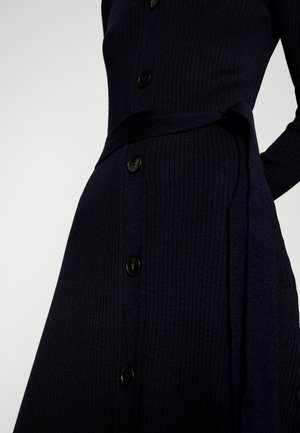 Zbliżenie na granatową, prążkowaną sukienkę dzianinową z czarnymi guzikami z przodu i pasem do wiązania w talii.