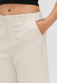 Pantaloni beige chiaro con una trama liscia, dotati di una tasca laterale, design dritto e una sottile cucitura decorativa in vita.