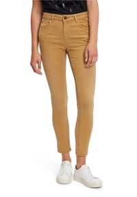 Tan skinny jeans with a smooth texture, five pockets, and a button closure. Paired with white sneakers.