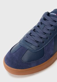 Mørkeblå sneakers med en kombinasjon av lær- og semsket skinnteksturer, med gummisåle og teksturerte snøringer, som har en avrundet tådesign.