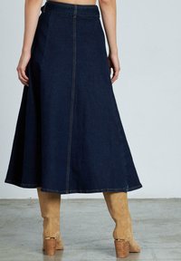 Falda de mezclilla en corte A de color azul oscuro con cintura alta, acentuada por costuras visibles y una costura trasera, combinada con botas largas de ante color caramelo.