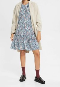 Blommig klänning i blått, rosa och grönt med en rynkad kjol, matchad med en ljusbeige kappa. Svarta loafers och bordeauxfärgade strumpor fulländar looken.