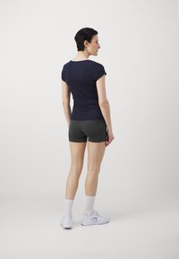 Marine idrettstopp med korte ermer, kombinert med mørkegrønne shorts. Hvite detaljer på halslinningen, brukt med hvite sneakers og ankelsokker.
