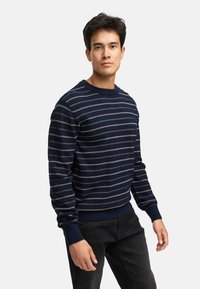 Marineblå strikket sweater med horisontale crème striber, rund hals, ribbede manchetter og kant, lavet af et blødt tekstureret stof.