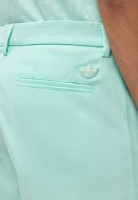 Ανοιχτό τιρκουάζ παντελόνια με πίσω τσέπη με γέμιση και κεντημένο λογότυπο Adidas, φορεμένα με αντίστοιχο τοπ με σχέδιο.