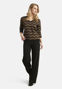 Black and gold V-neck sweater with zigzag pattern, paired with black wide-leg trousers and black shoes. Smooth texture and relaxed fit.