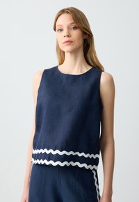 Navyfarbene Leinen-Ärmellose Bluse mit rundem Halsausschnitt und weißem, wellenförmigem Saum, der einen schichtartigen Effekt erzeugt. Glatte Textur.